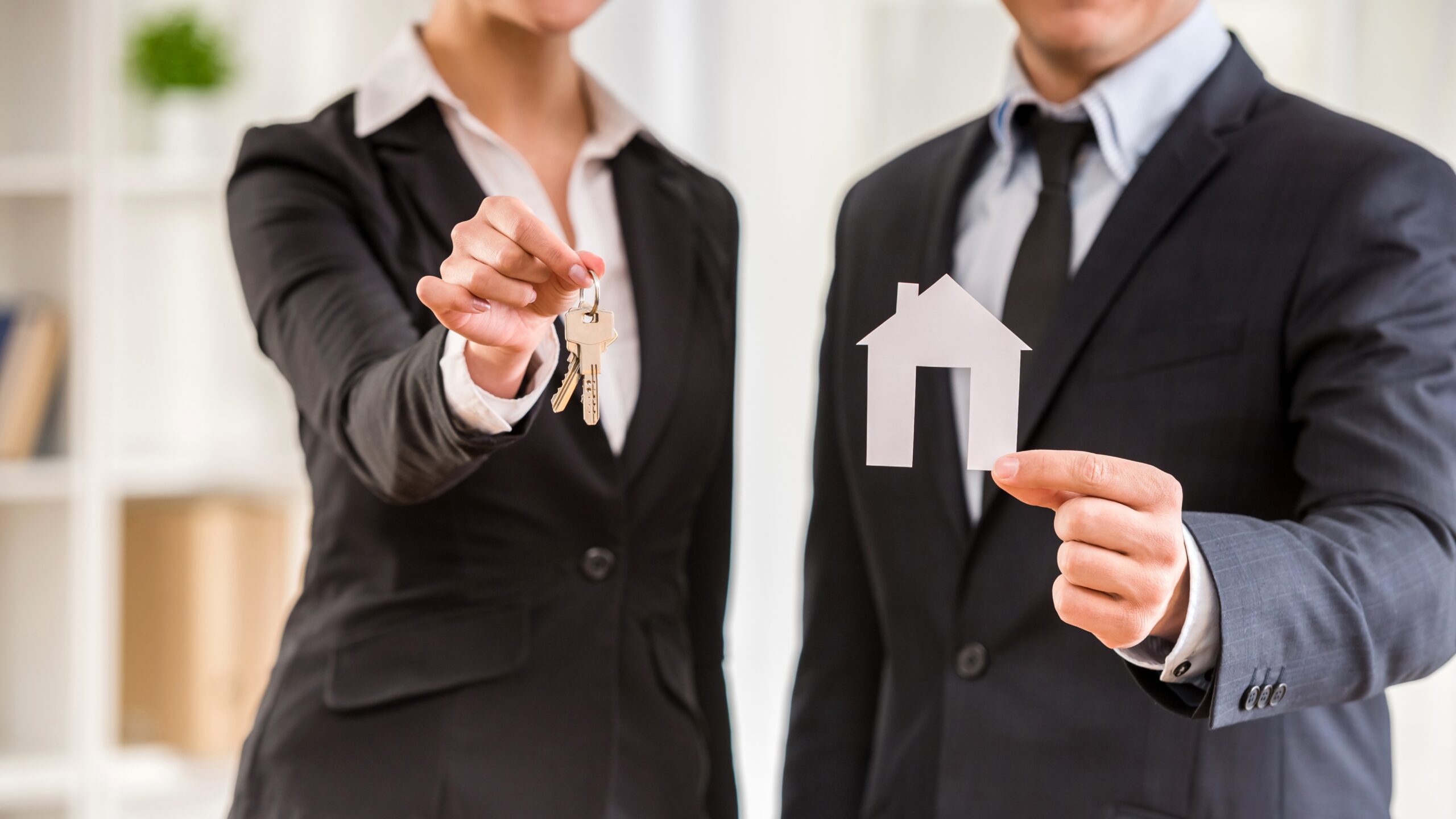 Two people holding a key and a small house