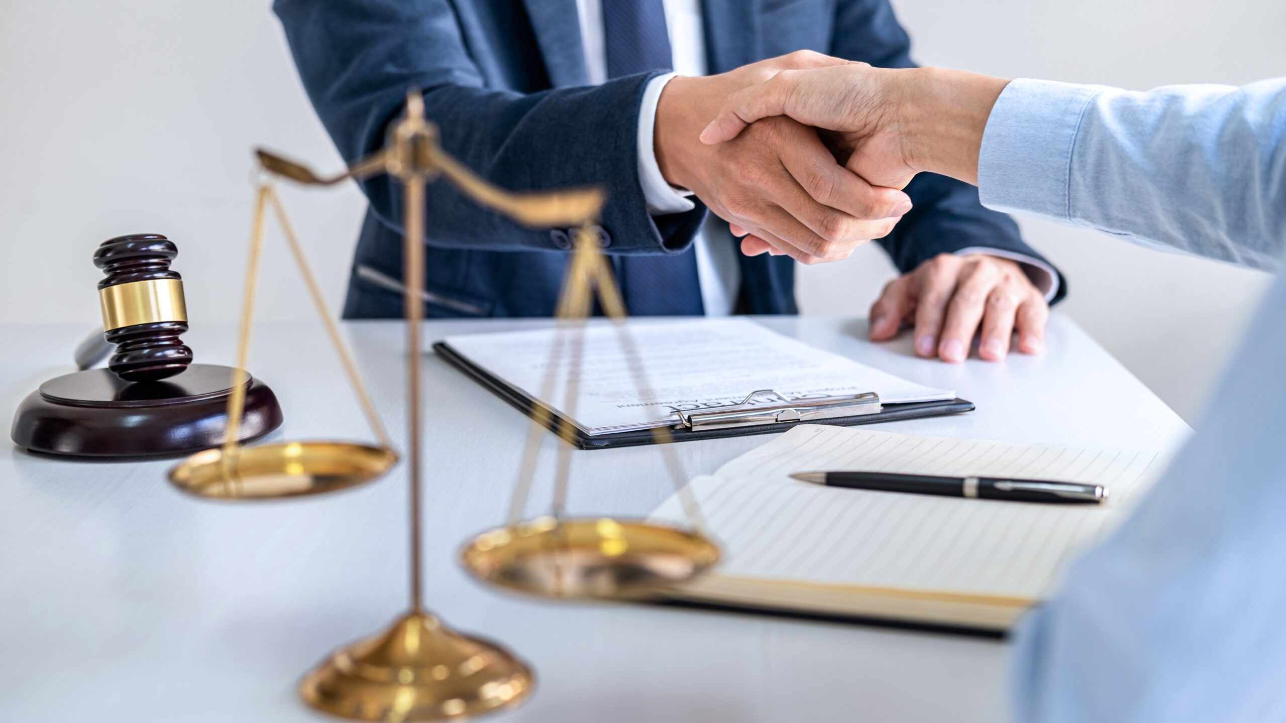 Двоє людей тиснуть руки під час юридичної угоди, поруч у фокусі молоток судді та терези правосуддя