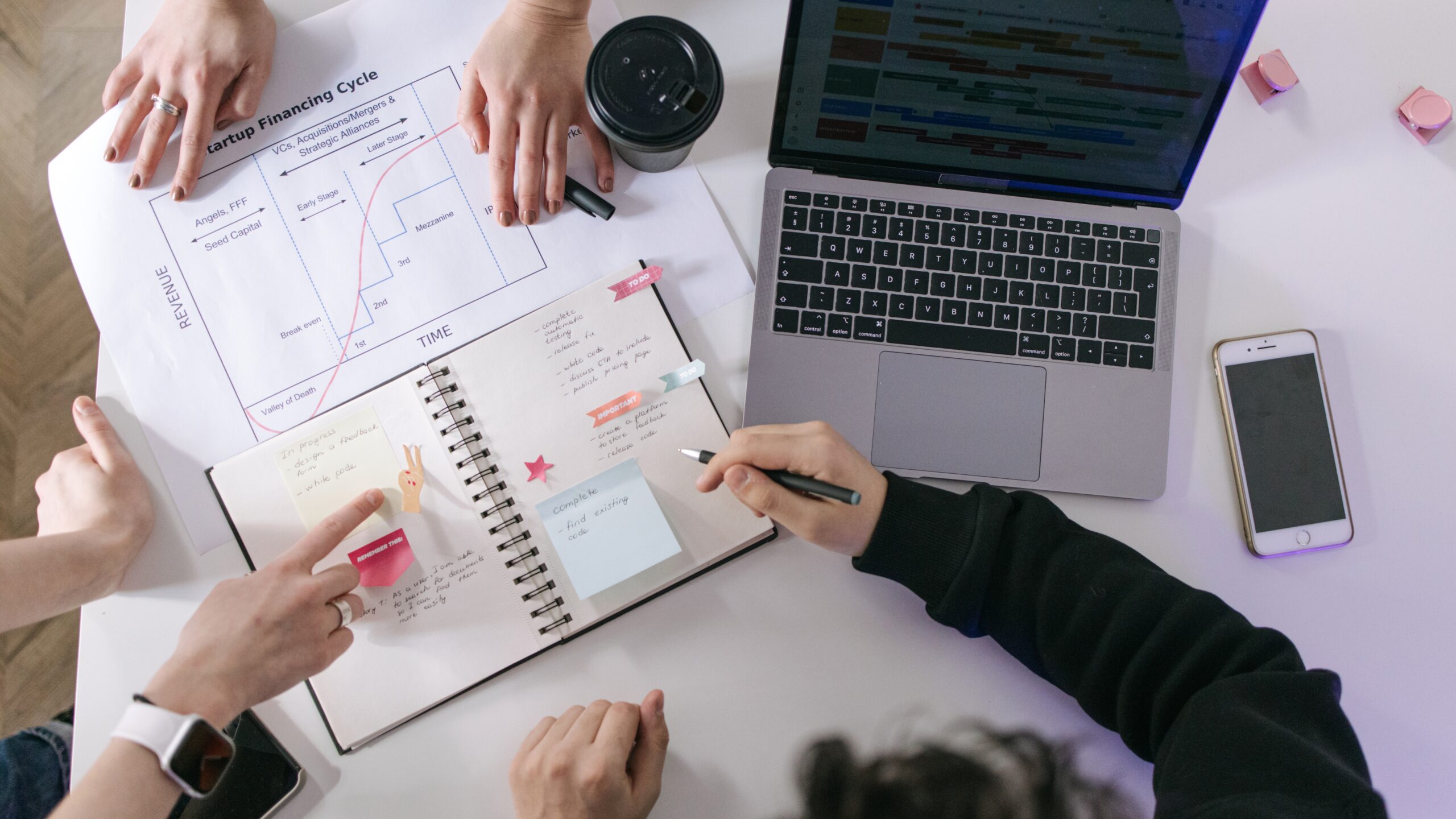 Three people reviewing charts, a laptop, and documents on a table while working on a startup